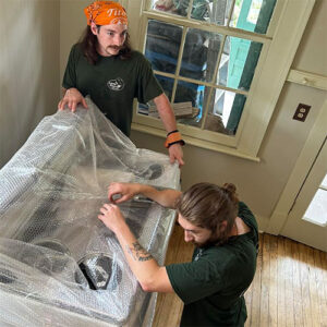 Two Ninaxandra Inc movers carefully wrap a large stove unit for transport.